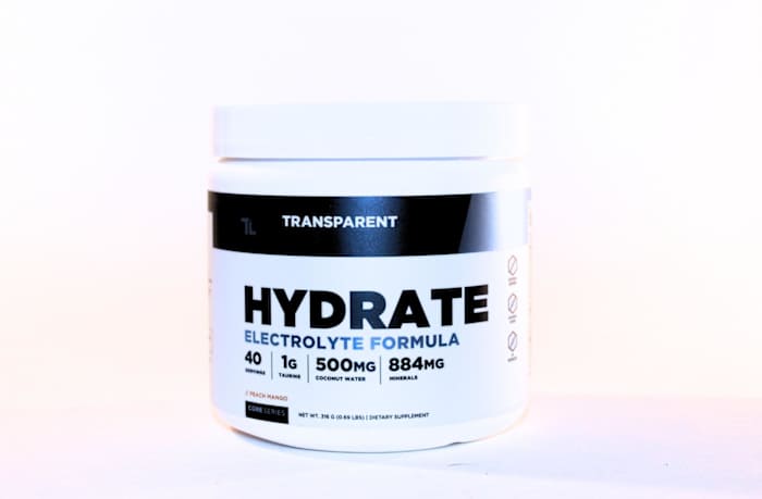 A white and black container of Transparent Labs Hydrate Electrolyte Formula in Peach Mango flavor against a white background